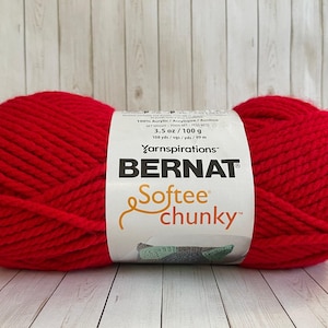 May include: A large ball of red Bernat Softee Chunky yarn. The yarn is wrapped with a white label that includes the brand name and product details. The yarn is 3.5 oz / 100 g and 108 yds / 99 m.