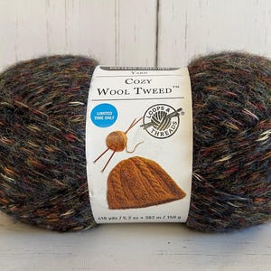 May include: A large ball of Cozy Wool Tweed yarn. The yarn is a mix of dark brown, red, yellow, and white fibers. The label reads "Cozy Wool Tweed" and includes a graphic of a knitted hat. The ball of yarn is 6.2 oz (176 grams).