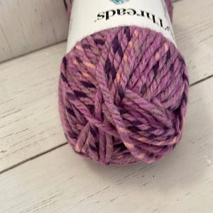 May include: A skein of pink, purple, and peach yarn with a white label that reads "Threads".