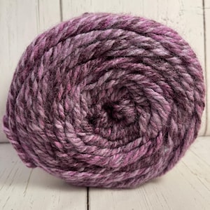 May include: A large ball of yarn in shades of purple, pink, and gray. The yarn appears thick and textured, ideal for knitting or crocheting projects. The colors blend together, creating a marbled effect.
