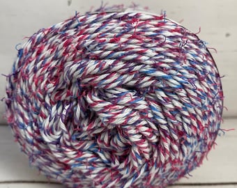 May include: A ball of white, pink, and blue yarn with a frayed texture. The yarn is twisted together in a spiral pattern.