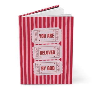 May include: A journal with a red and pink striped cover. The cover features three ticket-shaped designs with the words "YOU ARE BELOVED BY GOD" printed on them. The journal's pages are visible at the top.