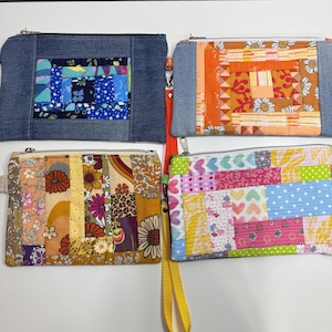 May include: Four handmade zippered pouches with patchwork designs. The pouches feature denim, floral, and patterned fabrics in various colors, including blue, orange, yellow, and pink. Each pouch has a different strap color, and a silver zipper.