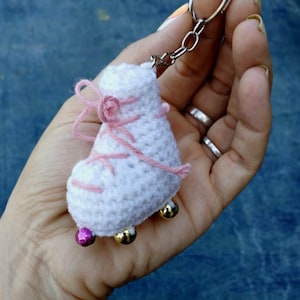 Op de afbeelding: Witte gehaakte rolstoelschlüsselhanger met roze veters en gouden en roze kralen.