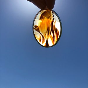 May include: A brown and white agate pendant with a silver setting. The pendant is oval shaped and has a swirling pattern.