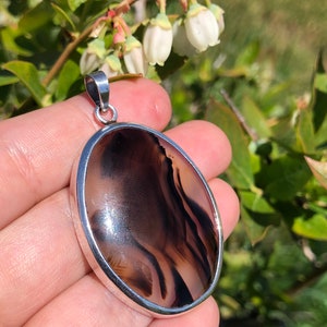 May include: A silver pendant featuring a brown and white agate stone. The stone has a swirling pattern of brown and white.