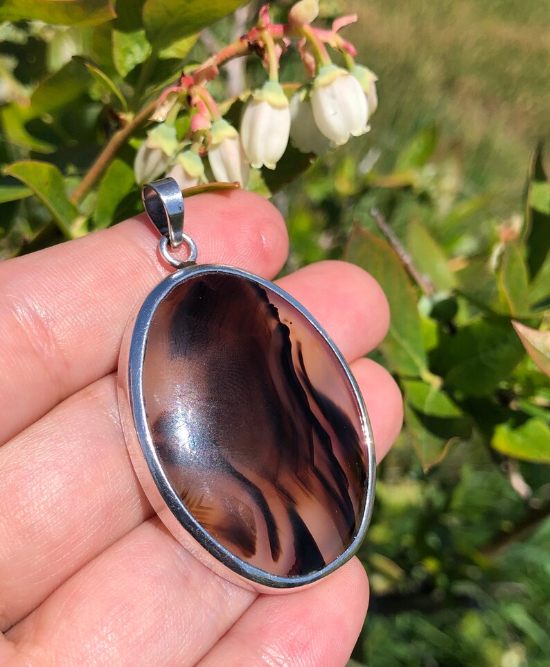 May include: A silver pendant featuring a brown and white agate stone. The stone has a swirling pattern of brown and white.