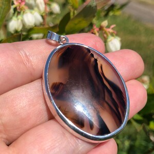 May include: A silver pendant featuring a brown and white agate stone. The stone displays a distinctive pattern of swirls and lines.