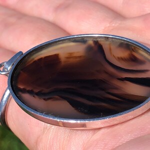 May include: A silver pendant featuring a round, brown agate stone. The stone displays a swirling pattern of light and dark brown.