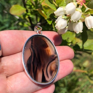 May include: A silver pendant featuring a brown and white agate stone. The stone has a swirling pattern.