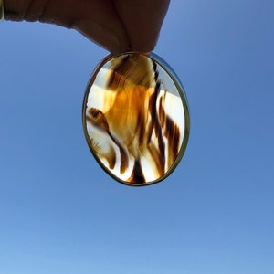 May include: A round, brown and white agate pendant with a silver setting. The agate has a swirling pattern of brown and white.