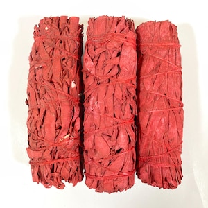 May include: Three cylindrical bundles of dried red sage leaves, each tightly wrapped with thin red string. The bundles are arranged vertically side-by-side, showcasing a uniform bright red color throughout the textured, layered plant material.