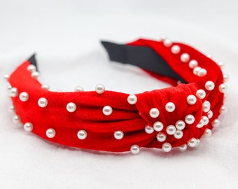 May include: Red velvet headband with a knotted design and white pearl embellishments.