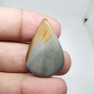 May include: A teardrop-shaped cabochon gemstone with a grey, brown, and yellow colour pattern.