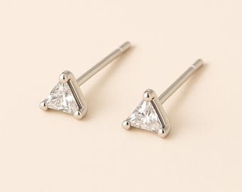 May include: A pair of silver stud earrings. Each earring features a clear, triangular-cut gemstone set in a silver frame. The earrings have a post and backing for secure wear. The background is a soft, neutral color.