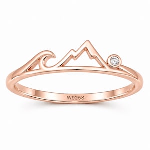 Könnte beinhalten: Roségoldener Ring mit Berg- und Wellendesign. Ein kleiner, klarer Edelstein ist in der Nähe des Berggipfels gesetzt. Der Ring ist mit "W925S" gestempelt.