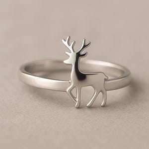 May include: A silver ring with a deer motif. The ring has a polished band and a detailed deer figure. The design is a simple, elegant piece of jewellery, suitable for everyday wear. The ring is made of a shiny, silver-coloured metal.