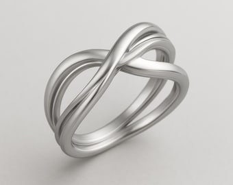 May include: A silver-colored ring with an intertwined design. The ring features a continuous, flowing pattern, with multiple bands that cross over each other. The metal has a smooth, polished finish, reflecting light. The ring is set against a neutral background.