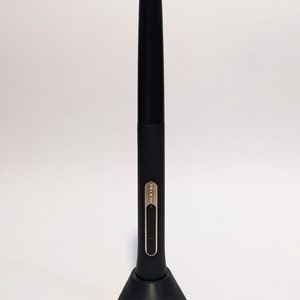 May include: A black stylus pen with a silver button and a black stand. The pen is designed for use with a digital tablet.