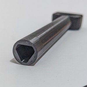 Può includere: Uno strumento in metallo nero con un'apertura a forma triangolare a un'estremità. Lo strumento è progettato per adattarsi a una forma specifica.