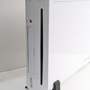 May include: A white Nintendo Wii U console with a disc drive slot, power button, eject button, and sync button. The console is sitting on a black stand.