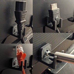 以下が含まれることがあります： 黒い表面に設置された黒いプラスチック製のケーブルオーガナイザーが4つあります。各オーガナイザーには、ケーブルを保持するためのフックが付いています。ケーブルには、黒い電源コード、黒いHDMIケーブル、赤いイーサネットケーブル、銀色の金属棒が含まれています。