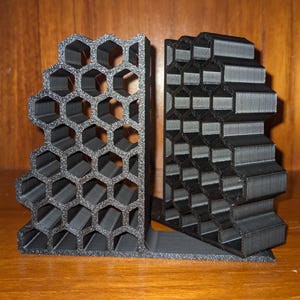 Op de afbeelding: Twee zwarte boekenleggers met een honingraatpatroon. De boekenleggers zijn gemaakt van 3D-geprint materiaal en hebben een geometrisch ontwerp.