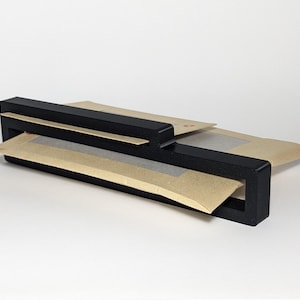 May include: A black, rectangular paper organiser with a slot for holding envelopes or small packages. The organiser is made of a solid, matte black material and is shown with several brown paper envelopes.