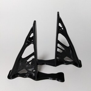 Puede incluir: Un soporte negro impreso en 3D con un diseño geométrico. El soporte está hecho de dos piezas que están conectadas entre sí.