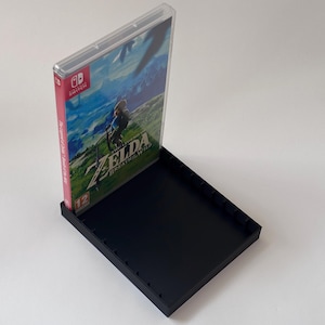 Op de afbeelding: Een zwarte plastic spelcase met een doorzichtige plastic hoes met een Nintendo Switch game cartridge. De spelcase is open en toont de cover art van het spel, met een personage in een bergachtig landschap. De game heet "The Legend of Zelda: Breath of the Wild".
