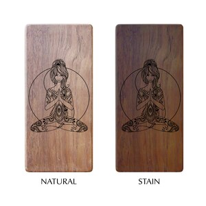 Op de afbeelding: Twee houten yogablokken, een naturel en een gebeitst, met een lasergegraveerd ontwerp van een vrouw in een yogapose. Het ontwerp heeft ingewikkelde details en een mandala-patroon.