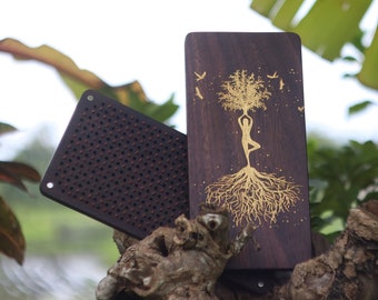 Könnte beinhalten: Eine Holzplakette mit einem goldfarbenen Design einer Frau, die in einem Baum steht, dessen Wurzeln sich ausbreiten. Die Plakette ist dunkelbraun und hat eine natürliche Holzmaserung. Kleine goldfarbene Vögel fliegen um den Baum herum.