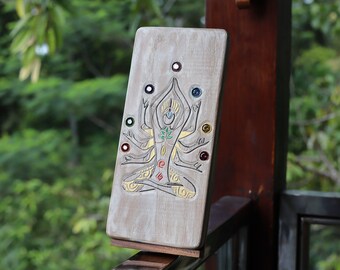 Könnte beinhalten: Eine Holztafel mit einer geschnitzten Abbildung einer Person in einer Yoga-Pose. Die Person hat sieben Chakren, die durch farbige Kreise dargestellt werden. Die Tafel steht auf einem Holzständer.