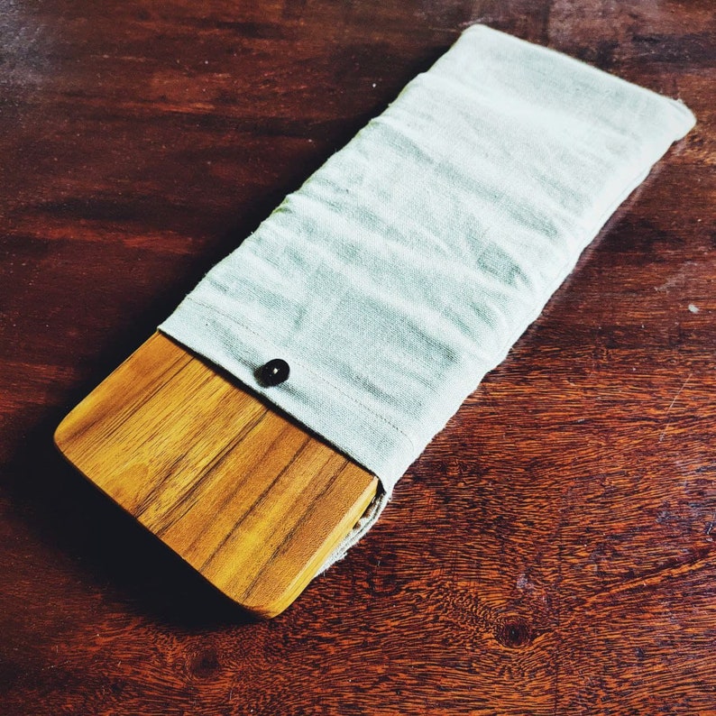 K&ouml;nnte beinhalten: Eine hellblaue Stofftasche mit einem Holzbrett zum Schneiden darin. Die Tasche hat einen Knopfverschluss und das Brett hat eine nat&uuml;rliche Holzmaserung.