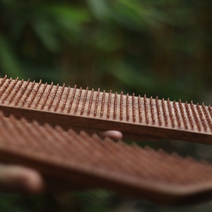 K&ouml;nnte beinhalten: Zwei Holzbretter mit Reihen kleiner, kupferfarbener N&auml;gel. Die Bretter werden in den H&auml;nden einer Person gehalten.