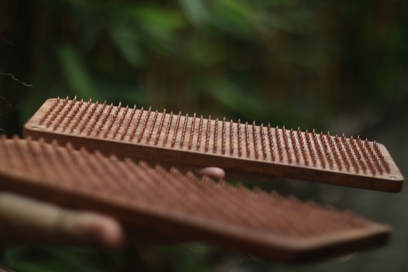K&ouml;nnte beinhalten: Zwei Holzbretter mit Reihen kleiner, kupferfarbener N&auml;gel. Die Bretter werden in den H&auml;nden einer Person gehalten.