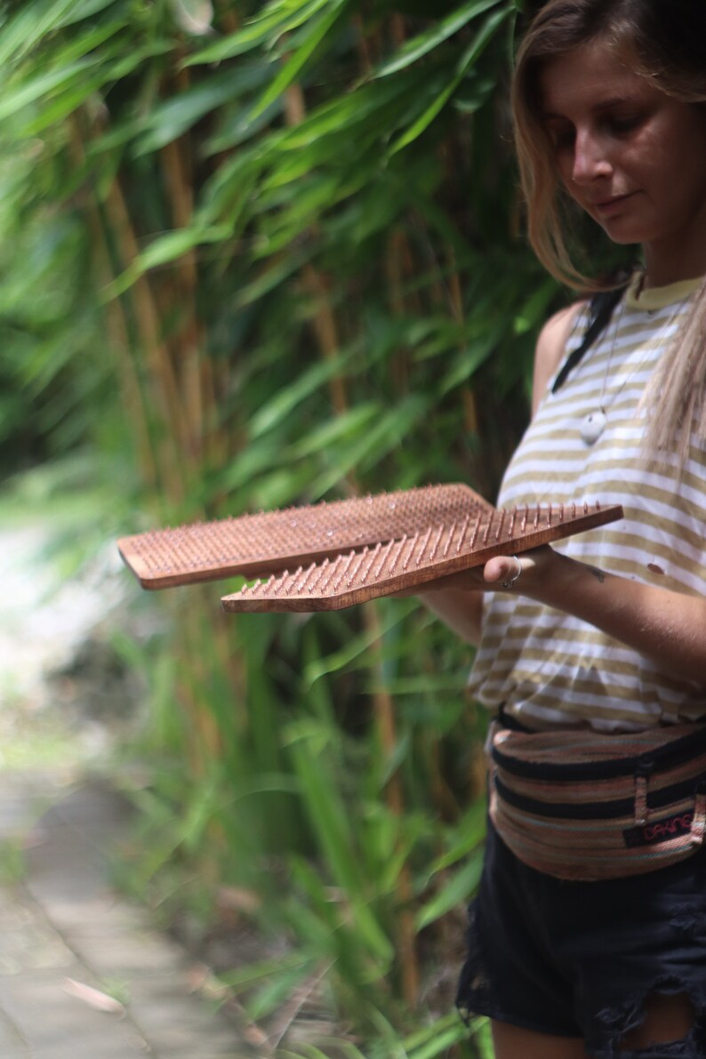 K&ouml;nnte beinhalten: Zwei Holzbretter mit Reihen kleiner, spitzer N&auml;gel. Die Bretter werden von einer Person gehalten, die ein gestreiftes Hemd und einen braunen G&uuml;rtel tr&auml;gt.