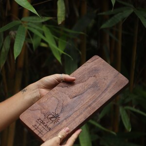 K&ouml;nnte beinhalten: Ein Schneidebrett aus Holz mit einer nat&uuml;rlichen Holzmaserung. Das Brett ist mit dem Text "Zdrava" und einem Logo mit einer Sonne und einem Buchstaben Z graviert. Das Brett wird von den H&auml;nden einer Person gehalten.