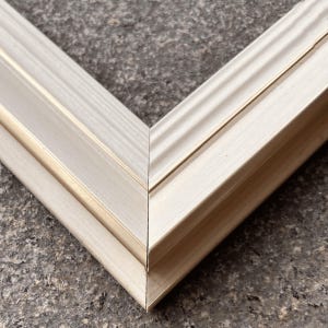 Pode incluir: Close-up de dois cantos conectados de uma moldura de madeira de cor clara. A moldura tem um design em camadas com uma superf&iacute;cie ligeiramente texturizada e um sutil detalhe dourado. Os cantos se encontram em um &acirc;ngulo preciso de 90 graus.