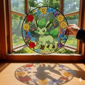Może przedstawiać: Okrągłe witrażowe okno przedstawiające zieloną postać z kreskówki otoczoną kolorowymi kwiatami i motylami. Okno jest obramowane czarną obwódką i wisi przed oknem z widokiem na drzewa.
