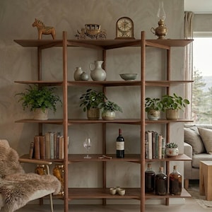 May include: A wooden bookshelf with multiple shelves displays various items. Decorative objects include a horse figurine, a carriage, a clock, and a lamp. Potted plants, books, wine bottles, and glassware are also arranged on the shelves, creating a stylish display.