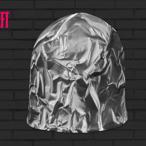 May include: A crumpled ball of aluminum foil, resembling a hat, against a black brick wall background.