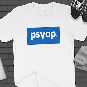 May include: White t-shirt with a blue rectangle that says "psyop" in white letters.
