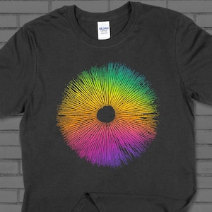 Puede incluir: Una camiseta gris oscuro con un diseño circular de colores. El diseño presenta un arcoíris de colores que irradian hacia afuera desde un centro negro.