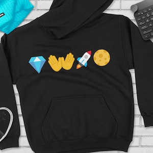 Puede incluir: Sudadera con capucha negra con un gráfico de diamante, dos manos, un cohete y una luna.
