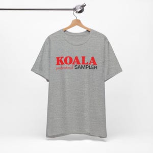 May include: A heather grey t-shirt with the text "KOALA professional SAMPLER" printed in red and black.
