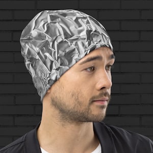 May include: A gray beanie with a crumpled foil pattern. The beanie is made of a soft, stretchy fabric and has a close-fitting design.
