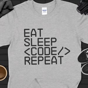 Puede incluir: Camiseta gris con el texto "Eat Sleep <Code/> Repeat" impreso en negro.
