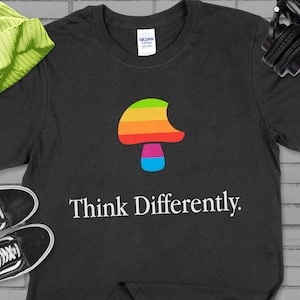May include: A dark grey t-shirt with a rainbow colored mushroom graphic and the text "Think Differently."