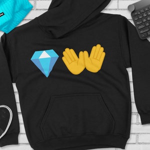 Puede incluir: Sudadera negra con un diamante azul y dos manos amarillas haciendo el signo 'W'.